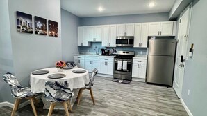 Une cuisine moderne avec des meubles blancs, des appareils en acier inoxydable et un coin repas comprenant une table ronde et des chaises.
