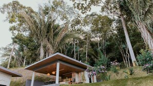 Un bâtiment moderne doté d’un espace extérieur couvert, entouré d’arbres et de verdure.