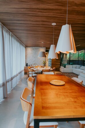 A modern dining area with a wooden table, white chairs, pendant lights, and a sofa in the background.
