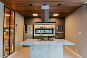 A modern kitchen with a central island, built-in appliances, and a wooden ceiling.