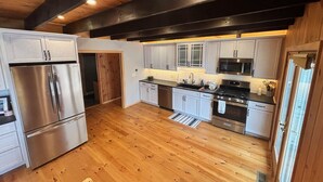 Una cocina moderna con electrodomésticos de acero inoxidable, piso de madera y una viga en el techo negra.