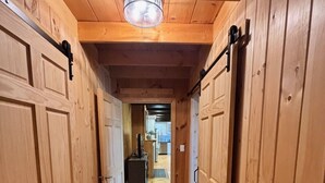 Un pasillo de madera con una lámpara en el techo, puertas de madera y vistas a una habitación con un refrigerador.