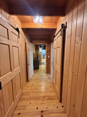 Ein Holzboden-Flur mit Deckenleuchte, Holztüren und Blick in einen Raum mit Kühlschrank.
