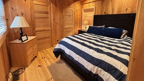 Un dormitorio con paneles de madera, una cama, mesitas de noche y una ventana.