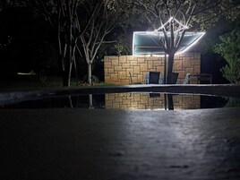 Vista nocturna de un edificio con fachada de piedra, una piscina al frente y asientos al aire libre.