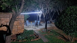 Een terras buiten met een stenen muur, een tafel met stoelen en een lichtslingering.