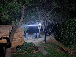 Un patio al aire libre con un muro de piedra, una mesa con sillas y una guirnalda de luces.