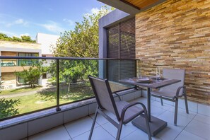 A balcony with a table and chairs, a view of greenery, and a modern building with a brick wall. - Studio c Piscina e Quadras em Barra de S o Miguel (Barra de São Miguel)