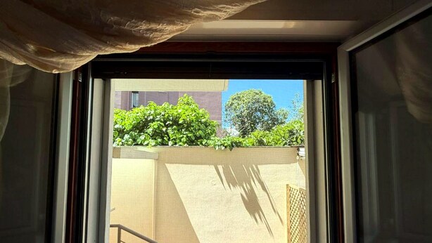Ein Fenster mit Blick auf ein Gebäudefassade, einem Metallgeländer und einem klaren Himmel.