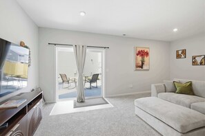 A living room with a sofa, a television, a sliding door to a balcony, and a painting on the wall. - New 4BR Ark + Creation Museum Hot Tub (Walton)