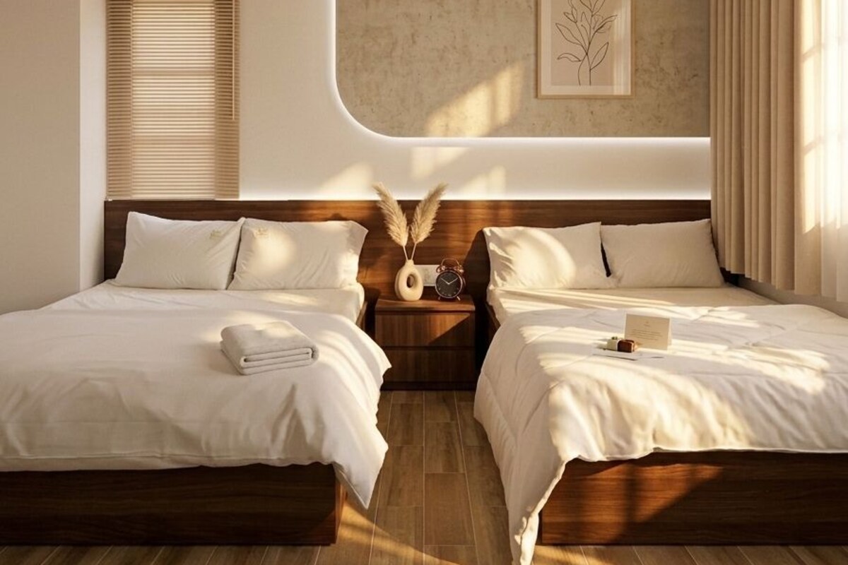 A modern bedroom with two beds, a wooden headboard, a bedside table with a clock, and a wall-mounted artwork.