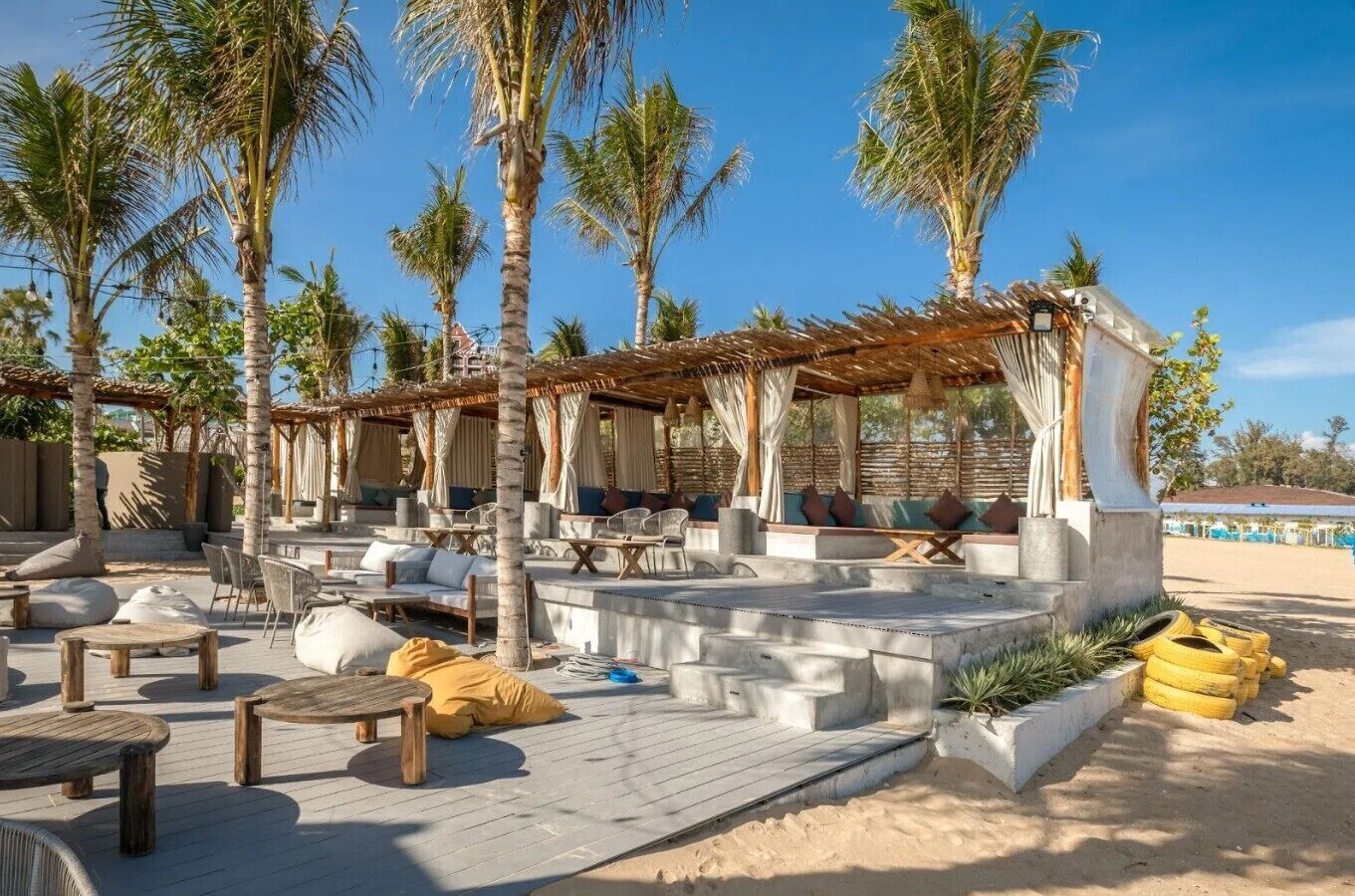 An outdoor lounge area with seating arrangements, palm trees, and a covered seating area.