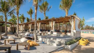 An outdoor lounge area with seating arrangements, palm trees, and a covered seating area.