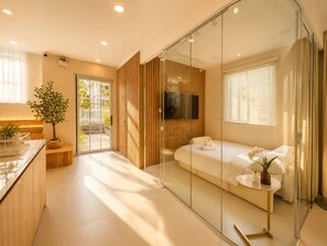 A modern bedroom with a glass partition, a bed, a TV, and a small table. - Novaworld Phan Thiet - Mira Villas (Tien Thanh)