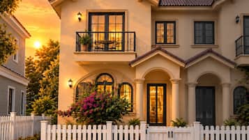 A two-story house with a balcony, a white picket fence, and a well-maintained garden.