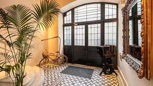 En hall med ett mönstrat golv, en stor spegel, en cykel och en dörr med frostade glaspaneler.