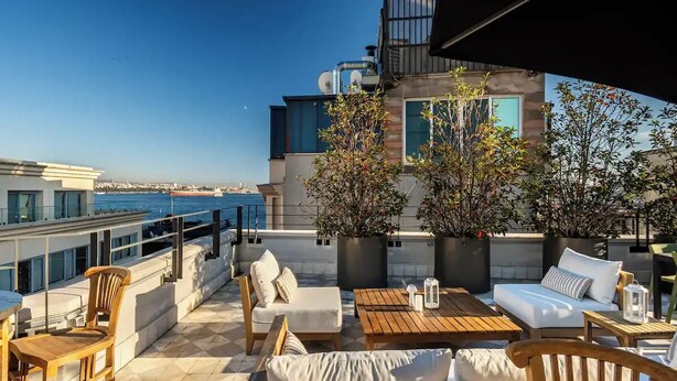 Terraço no telhado com área de estar ao ar livre, vista para o mar e um edifício com varanda.