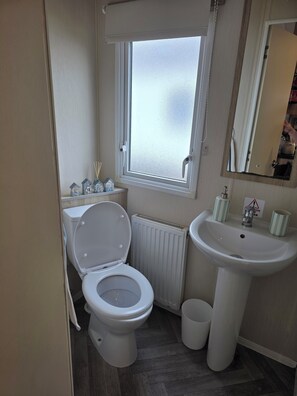 A bathroom with a toilet, a sink, a window, and a mirror.