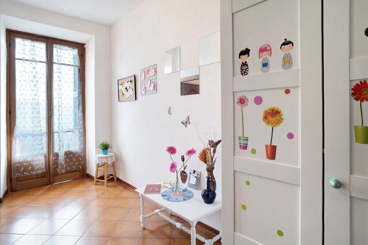 Een kamer met een witte wand, een klein tafeltje met decoratieve objecten, een deur met een raam en een plank met beeldjes.