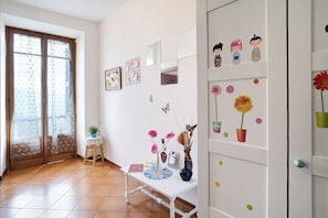 A room with a white wall, a small table with decorative items, a door with a window, and a shelf with figurines. - Divine Villa Viani (Villa Viani)