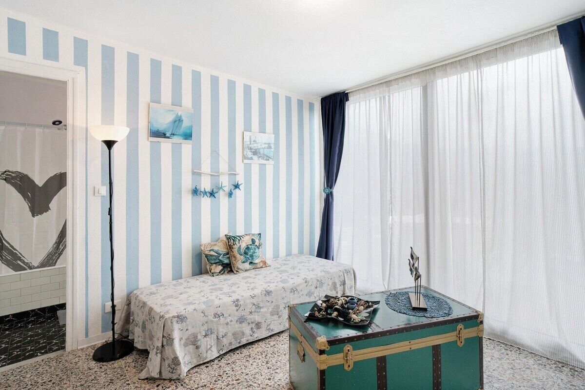 A room with striped walls, a bed, a small table, and a window with curtains.