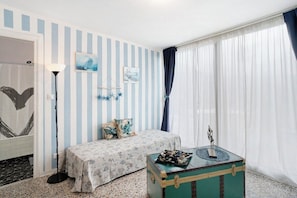 A room with striped walls, a bed, a small table, and a window with curtains. - Divine Villa Viani (Villa Viani)