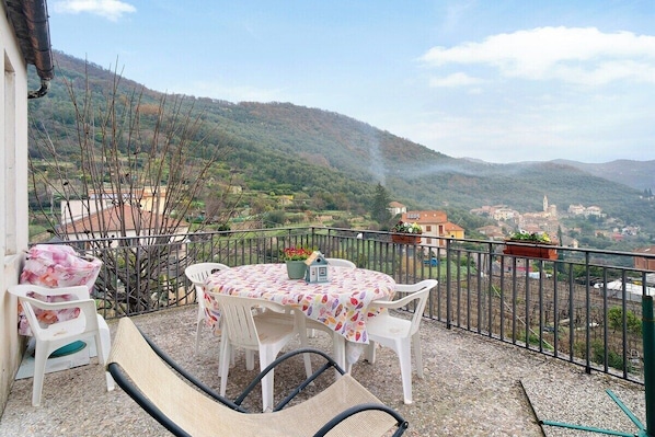 A balcony with a table and chairs, overlooking a mountainous landscape. - Divine Villa Viani (Villa Viani)