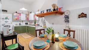 Una cocina con armarios verdes, una mesa de comedor de madera con platos azules y un estante colgante con diversos utensilios de cocina.