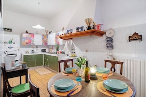 A kitchen with green cabinets, a wooden dining table with blue plates, and a hanging shelf with various kitchen items. - Divine Villa Viani (Villa Viani)