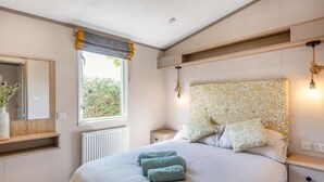 Ein Schlafzimmer mit einem großen Bett, Nachttischen, einem Spiegel und einem Fenster mit Vorhängen.