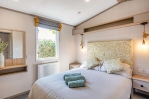Ein Schlafzimmer mit einem großen Bett, Nachttischen, einem Spiegel und einem Fenster mit Vorhängen.