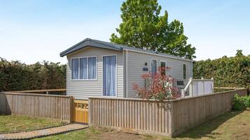 A single-story mobile home with a fenced yard, a small porch, and a tree in the background.