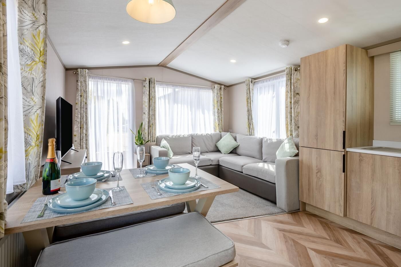 A modern living room with a sofa, a dining table set for two, and a kitchen area with cabinets.