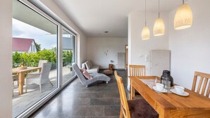 A modern interior with a dining area, a lounge chair, and a large glass door leading to an outdoor patio.
