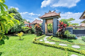 Ein traditionelles Gebäude mit einem Ziegeldach, umgeben von einem gepflegten Garten mit Kieswegen und üppiger Vegetation.