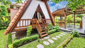 Een boomhut met een houten trap, een overdekt terras en een tuin met sierpaden.