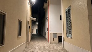 Ein schmaler Gang mit Fliesen, einer Straßenlaterne und Gebäuden mit Balkonen und Fensterläden.
