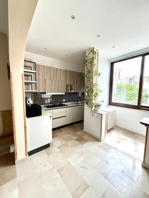 Una cucina moderna con piano cottura integrato, mobili bianchi e una finestra vista edifici.