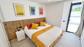 A bedroom with a wooden headboard, a bed with yellow and red pillows, a white bedside table, and a nightstand. There are three framed artworks on the wall above the bed. - SUN SEA & LOVE: Beachfront villa 33 meters from the sand (Puerto Rico)