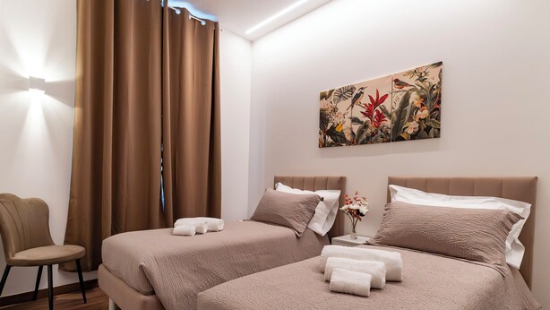 A hotel room with two beds, a chair, a painting, and a nightstand with a vase. - Cozy twin room with private bathroom. (Livorno)