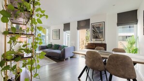 A modern living room with a sofa, dining table, and chairs. There is a large window with a view of the outside. - Sleek 1BDR Flat with Balcony Private Work Space (Greater London)