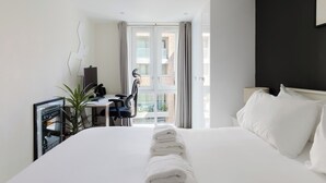 A hotel room with a large bed, a desk with a chair, a TV, and a view of the outside. - Sleek 1BDR Flat with Balcony Private Work Space (Greater London)