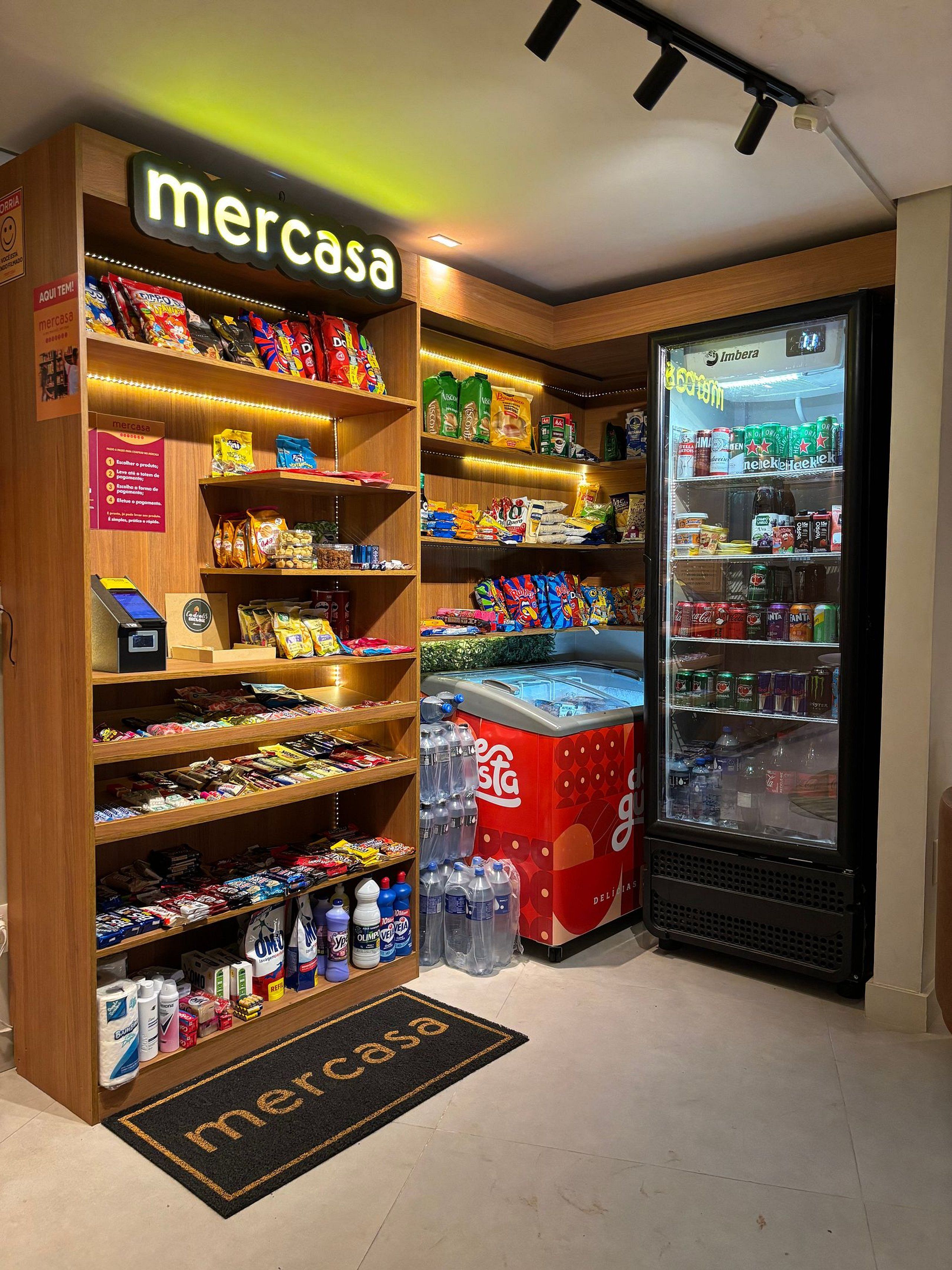 Uma loja Mercasa com prateleiras repletas de petiscos, um refrigerador de Coca-Cola e um balcão refrigerado.