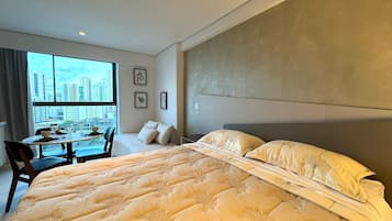 Quarto de hotel com uma cama grande, área de refeições e vista para a cidade.