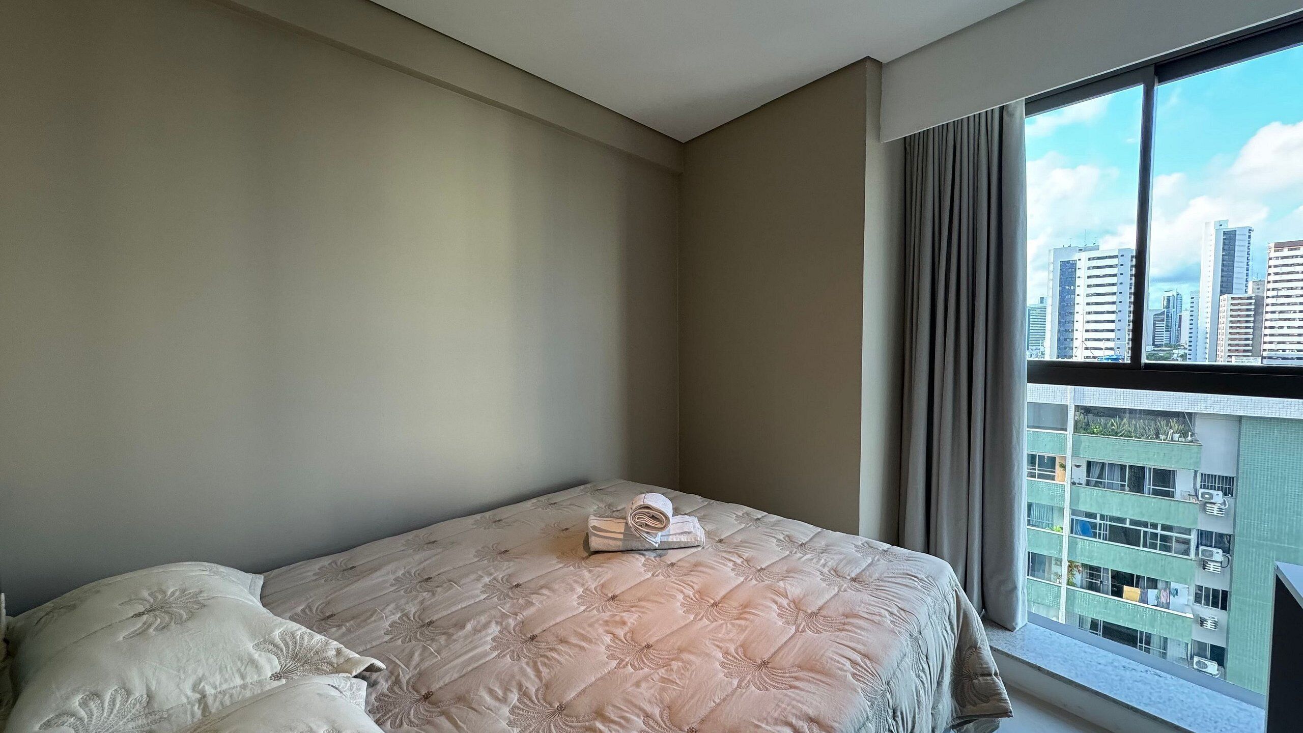 A bedroom with a bed, pillows, and a window with a city view.