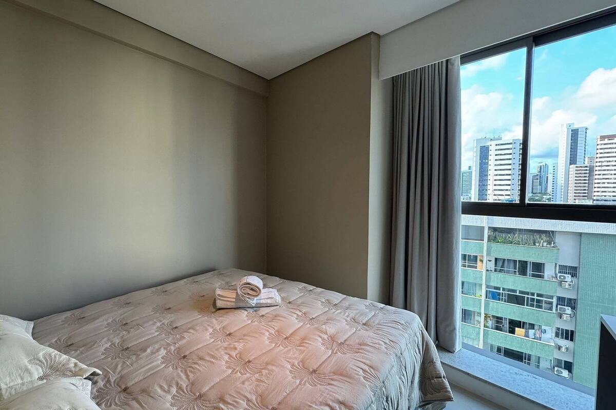Quarto com cama, almofadas e janela com vista para a cidade.