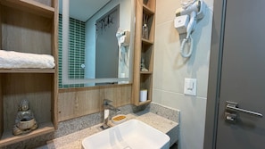 A bathroom with a sink, mirror, hairdryer, and shelves with toiletries.