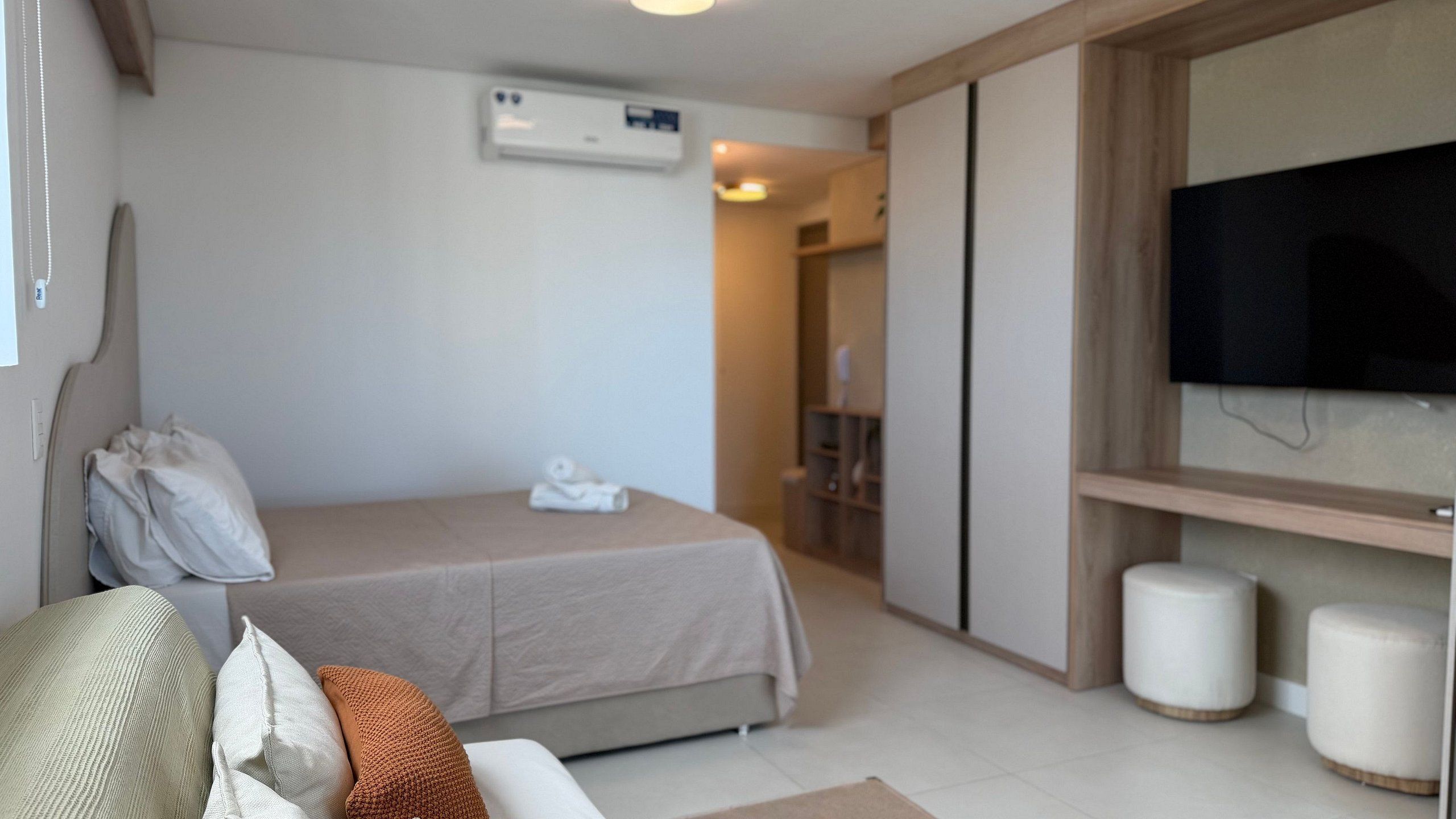 A hotel room with a bed, a TV, a wardrobe, and a bathroom visible in the background.