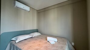 En säng för en person med en sänggavel, en hoprullad handduk och en luftkonditioneringsanläggning som är monterad på väggen.