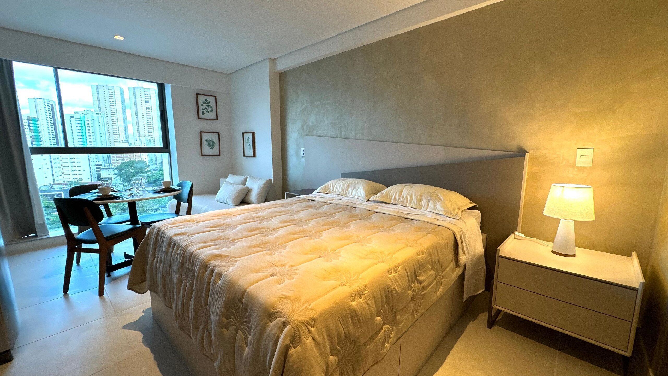 A hotel room with a large bed, bedside table, and a view of the cityscape.